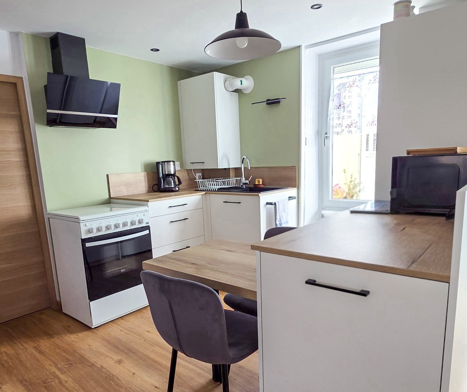 Cuisine rénovée d'une maison familiale, mur vert sauge et plan de travail en bois